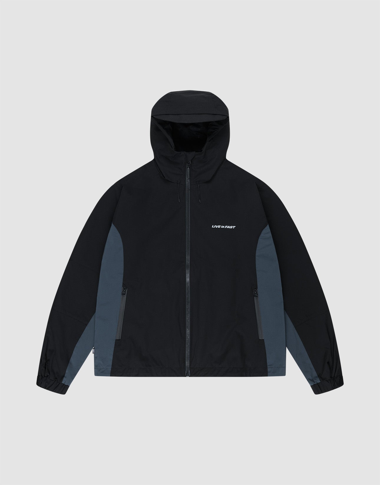 The LIVE FAST DIE YOUNG Basic Shell Jacket features an oversize fit, black hood, dark gray panels, front zipper, side pockets, and "LMC PDRF" in small white letters on the left chest. Shown laid flat on a light gray background.