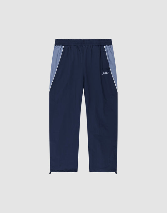 LIVE FAST DIE YOUNG Basic Nylon Trackpants in navy blue feature light blue hip panels, white piping along zip pockets, an elastic waistband, drawstring ankles, and a small white logo on the left thigh, shown flat on a light gray background.