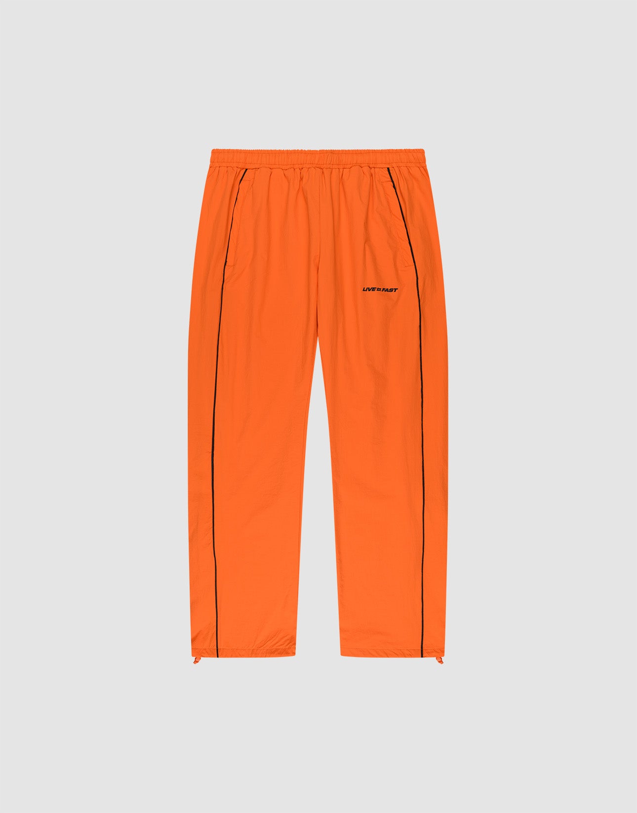 The LIVE FAST DIE YOUNG Live Fast Trackpants feature a bright orange wide-fit design with an elastic waistband, black vertical leg piping, side pockets, and a reflective logo print on the left thigh, presented on a plain light gray background.