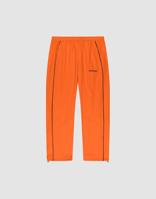 The LIVE FAST DIE YOUNG Live Fast Trackpants feature a bright orange wide-fit design with an elastic waistband, black vertical leg piping, side pockets, and a reflective logo print on the left thigh, presented on a plain light gray background. | plain