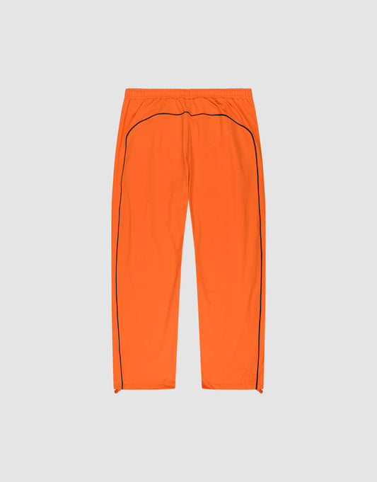 The LIVE FAST DIE YOUNG Live Fast Trackpants are bright orange, wide fit with an elastic waistband, black side piping, and a reflective logo print, shown flat on a light gray background.