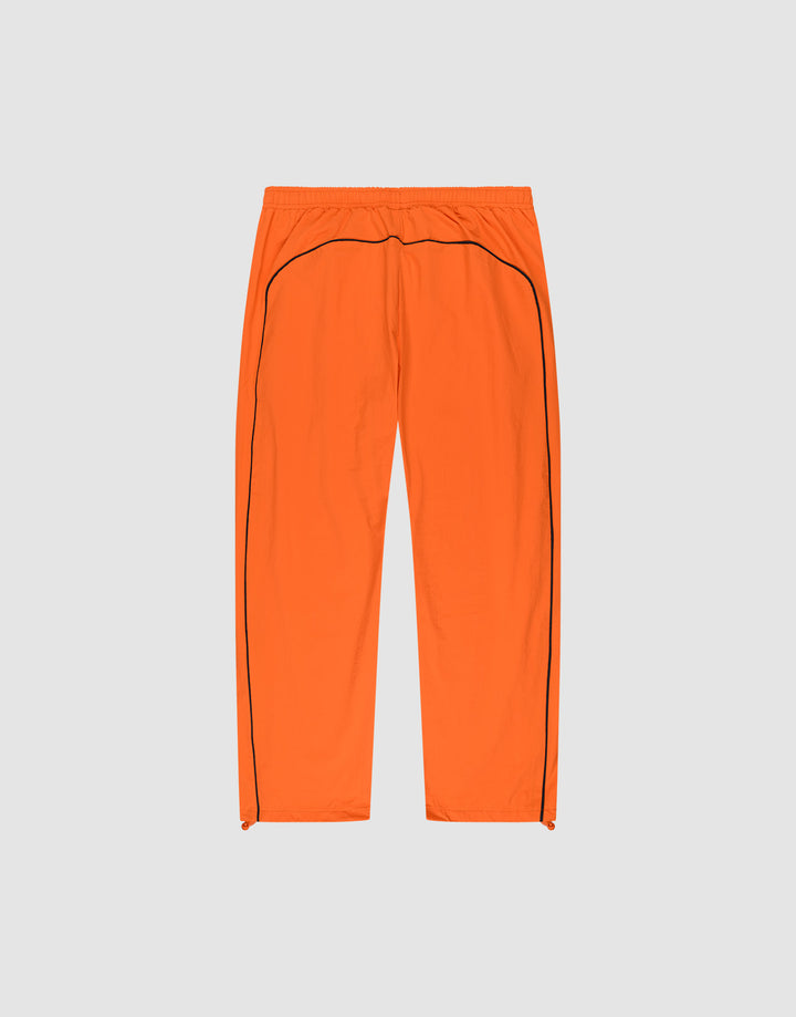 The LIVE FAST DIE YOUNG Live Fast Trackpants are bright orange, wide fit with an elastic waistband, black side piping, and a reflective logo print, shown flat on a light gray background.