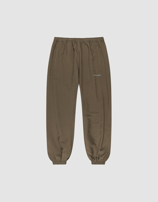 The LFDY Trackpants by LIVE FAST DIE YOUNG feature a regular fit, elastic waistband and cuffs, two side pockets, and a small reflective white logo on the left thigh. Made from soft polyester, shown on a light gray background. | plain