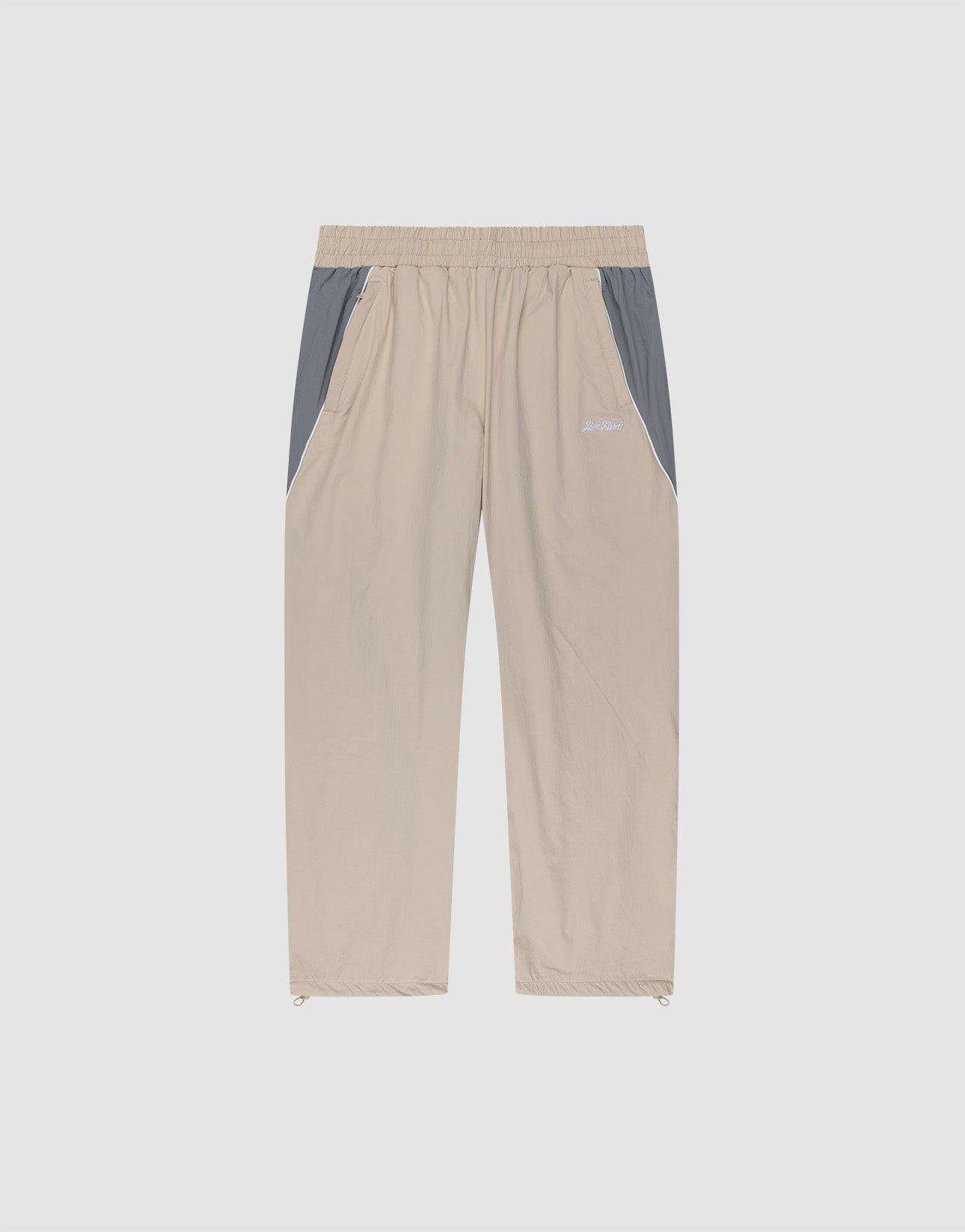 LIVE FAST DIE YOUNG Basic Nylon Trackpants in beige with grey side panels, elastic waistband, side pockets, and elasticated cuffs, displayed flat on a plain light background.