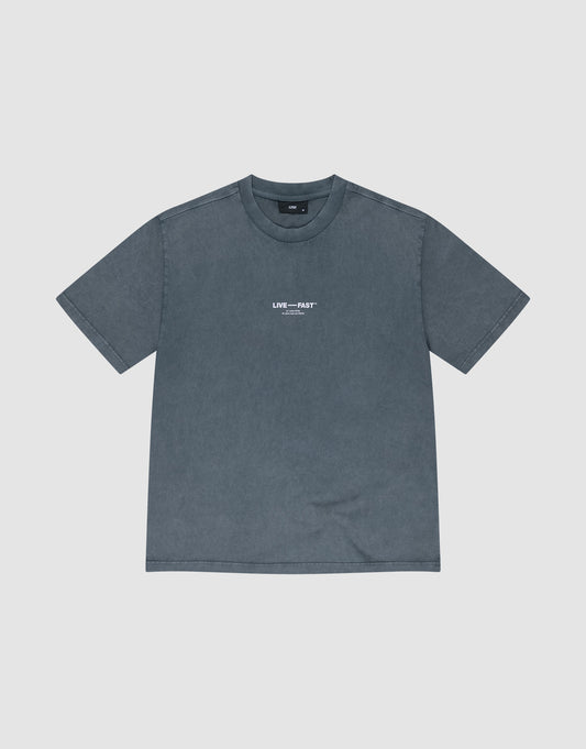 The It's Vulgar Tee by LIVE FAST DIE YOUNG is an oversize, short-sleeved, faded blue-gray T-shirt made of 100% Baumwolle, featuring small white "LIVE---FAST" text on the chest and shown laid flat on a light background.