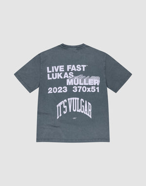 The It's Vulgar Tee by LIVE FAST DIE YOUNG is a dark gray, 100% cotton oversized T-shirt with white front text and a blurred car back print reading "LIVE FAST LUKAS MÜLLER 2023 370x51 ITS VULGAR. | plain
