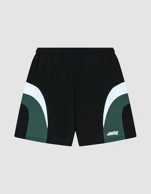 The LIVE FAST DIE YOUNG Basic Trackshorts feature a black oversize fit with dark green and white curved color block side accents, an elastic waistband, and a small white logo print on the lower left leg. Displayed on a light gray background. | plain