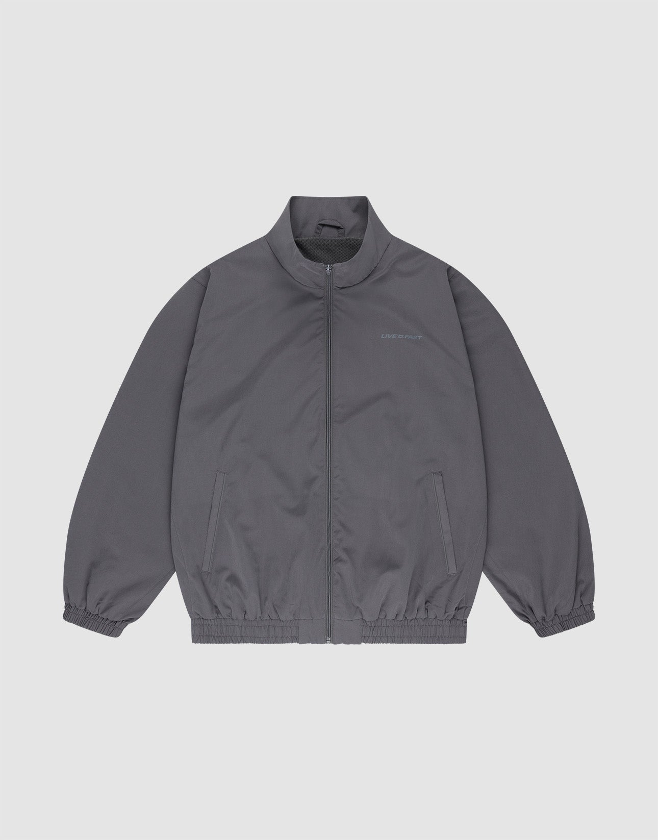 The LFDY Trackjacket by LIVE FAST DIE YOUNG is a gray polyester zip-up with a stand collar, elastic cuffs and hem, oversize fit, chest text detail, and two side pockets, shown on a plain white background.
