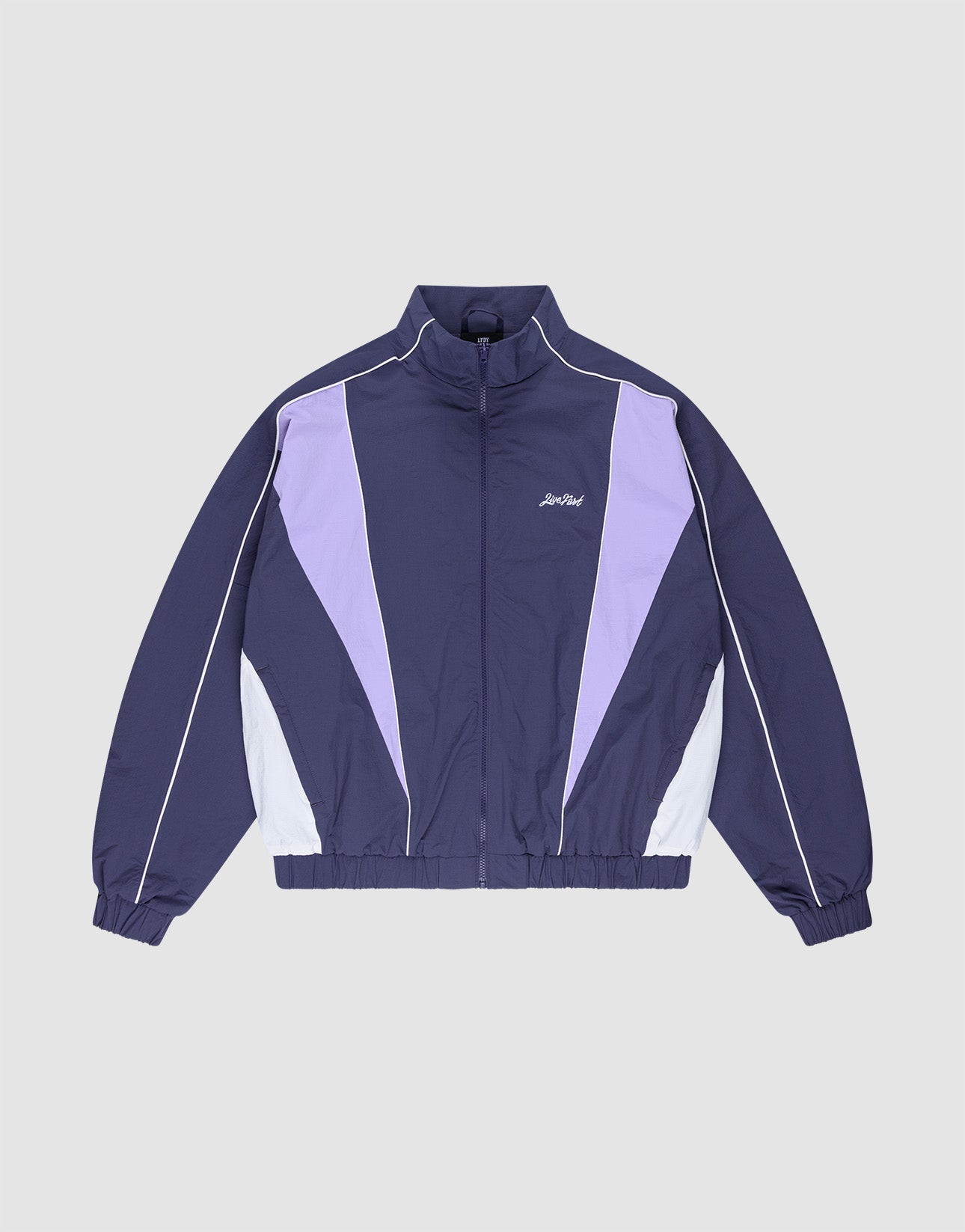 The LIVE FAST DIE YOUNG Basic Nylon Trackjacket features a navy blue and lavender Regular Fit with white accents, a zip-up front, high collar, Logo-Stick detail, and elastic cuffs and hem, shown on a light gray background.