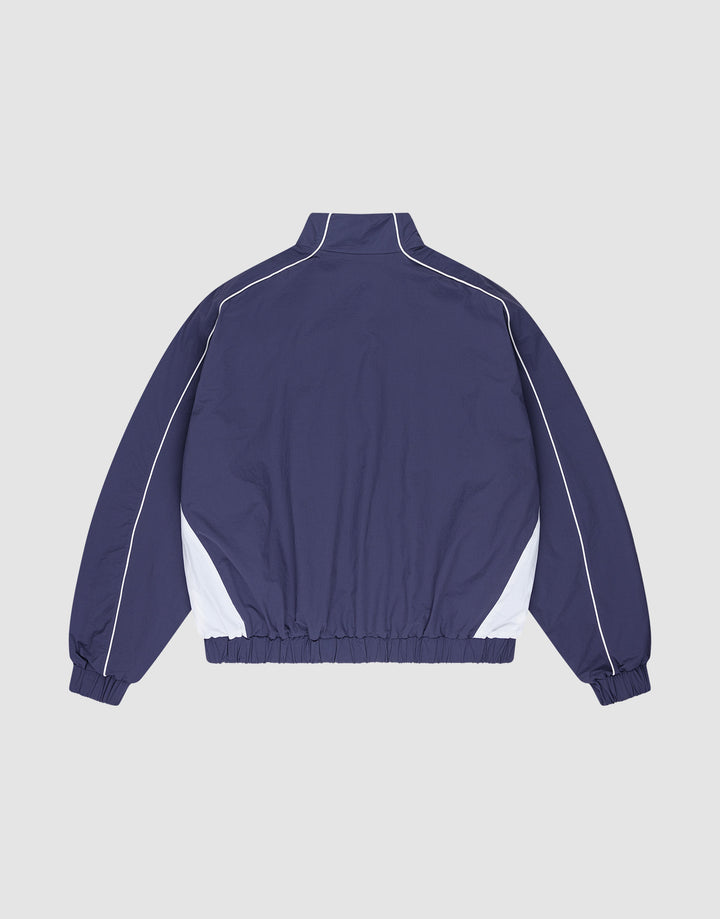 The LIVE FAST DIE YOUNG Basic Nylon Trackjacket in navy blue features a regular fit, white side panels and piping, high collar, elastic waistband and cuffs, plus a subtle logo-stitch detail. Shown on a plain light gray background.