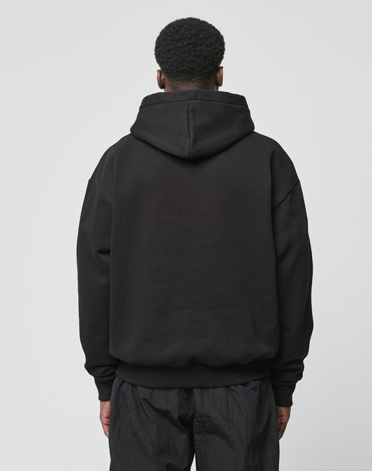 A person with short, curly hair is seen from behind wearing the LIVE FAST DIE YOUNG Live Fast Garment Hooded sweatshirt in black with black pants, set against a plain light background.