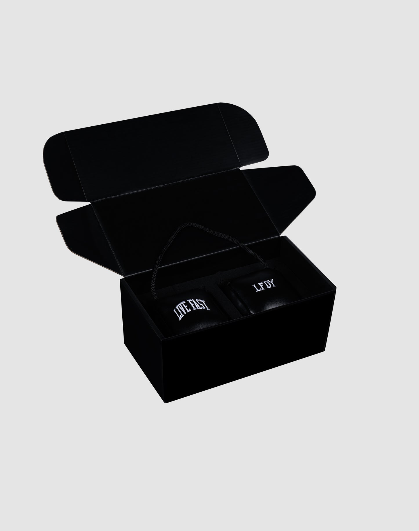 A black gift box with its lid open reveals two black LFDY Leather Car Dice by LIVE FAST DIE YOUNG inside, each labeled "LITE BOX" in white text. The box rests on a plain light gray background.