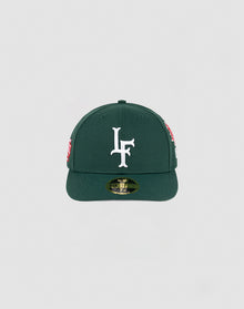 The LFDY x NEW ERA 59FIFTY Low Profile by LIVE FAST DIE YOUNG is a dark green fitted cap with a flat brim, large white LF logo on the front, side patches, and a gold sticker on the brim.