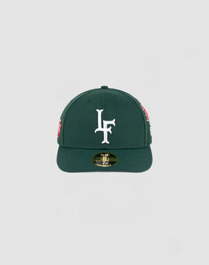 The LFDY x NEW ERA 59FIFTY Low Profile by LIVE FAST DIE YOUNG is a dark green fitted cap with a flat brim, large white LF logo on the front, side patches, and a gold sticker on the brim.