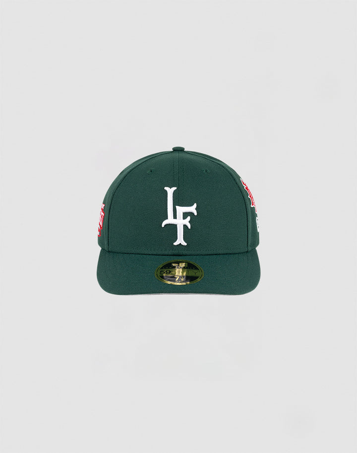 The LFDY x NEW ERA 59FIFTY Low Profile by LIVE FAST DIE YOUNG is a dark green fitted cap with a flat brim, large white LF logo on the front, side patches, and a gold sticker on the brim.