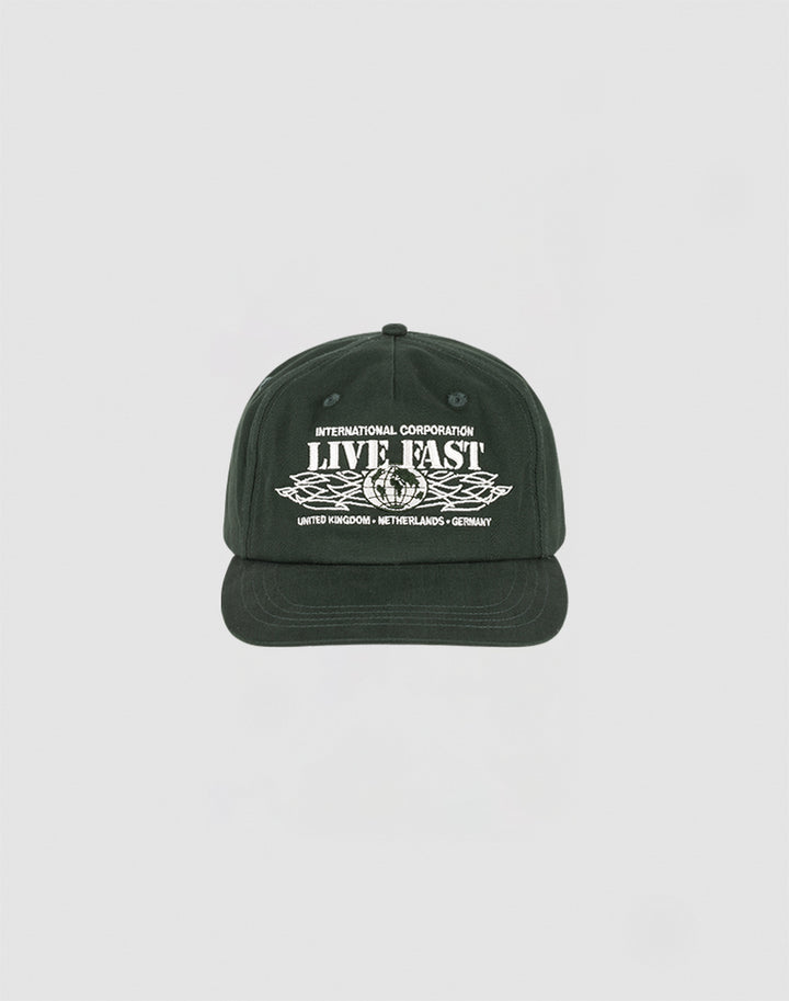 The Live Fast Corporation Cap by LIVE FAST DIE YOUNG is a black 5-panel cap with white INTERNATIONAL CORPORATION LIVE FAST text above wings and country names below, featuring a Multi-Logo design on a plain light background.
