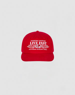 The Live Fast Corporation Cap by LIVE FAST DIE YOUNG is a 100% cotton red cap with bold white International Corporation LIVE FAST text and multi-logo graphics, plus country names United Kingdom, Netherlands, and Germany on the front.