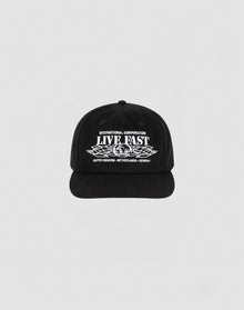 The Live Fast Corporation Cap by LIVE FAST DIE YOUNG is a black, 100% cotton unstructured 5-panel hat with multi-logo white text and graphics reading INTERNATIONAL CORPORATION LIVE FAST above stylized wings and UNITED KINGDOM - NETHERLANDS - GERMANY below.