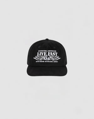 The Live Fast Corporation Cap by LIVE FAST DIE YOUNG is a black, 100% cotton unstructured 5-panel hat with multi-logo white text and graphics reading INTERNATIONAL CORPORATION LIVE FAST above stylized wings and UNITED KINGDOM - NETHERLANDS - GERMANY below.