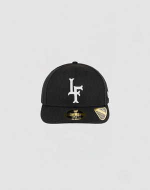 The LFDY x NEW ERA 59FIFTY Low Profile by LIVE FAST DIE YOUNG is a black fitted cap with a white LF logo on the front, gold sticker on the brim, and small white side logo, shown against a plain light gray background.