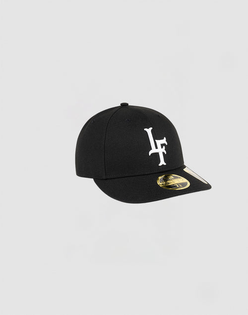 The LFDY x NEW ERA 59FIFTY Low Profile by LIVE FAST DIE YOUNG is a black fitted cap with a white LF logo on the front and a gold sticker on the brim, displayed against a plain light gray background.
