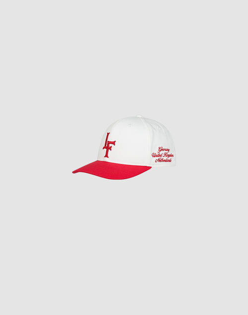 The LF Snapback by LIVE FAST DIE YOUNG is a white cap with a red brim and red LF logo-stick embroidery on the front, plus red script text on the side. Made from 100% Baumwolle, it features a snap closure. Light gray background.