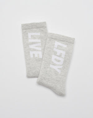 Two light gray Basic Typo Socks (2 Pack) from LIVE FAST DIE YOUNG, each with a bold white LIVE and LF DY logo arranged vertically, overlap on a plain white background.