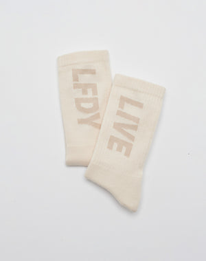 The LIVE FAST DIE YOUNG Basic Typo Socks (2 Pack) in off-white feature the LFDY logo on one sock and LIVE on the other, shown against a plain white background.