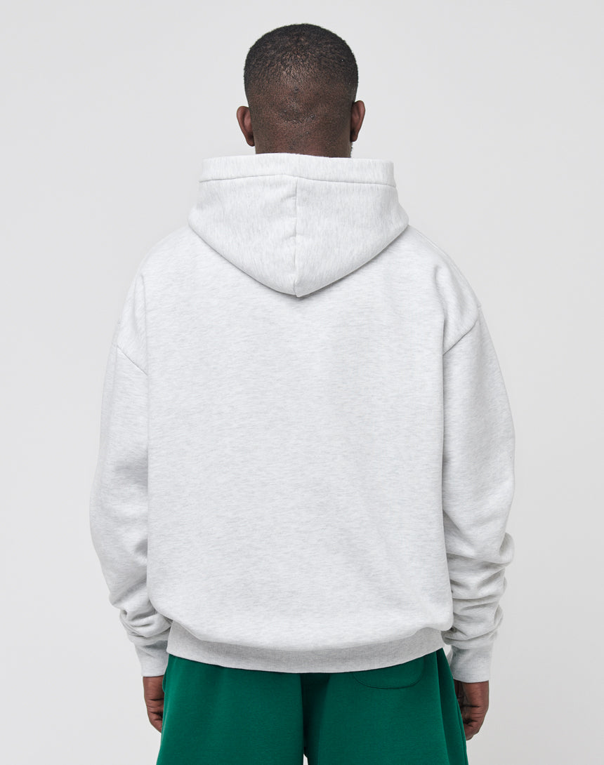 A person stands with their back to the camera, wearing a light gray LIVE FAST DIE YOUNG Basic Wrist Hooded with the hood down and green pants. The plain, light background highlights the relaxed vintage effect of their outfit.