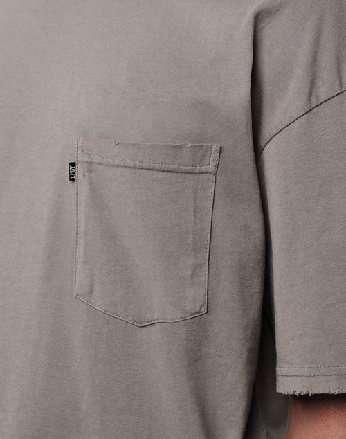 Close-up of the LFDY Destroyed Pocket Tee, a gray oversize T-shirt with a left chest pocket. The pocket has a small black tag on its edge. Made from soft plain fabric, it features visible seam details for added comfort.