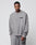 A man stands against a plain background wearing the LIVE FAST DIE YOUNG Basic Chest Sweater and matching sweatpants in light gray. Both feature topstitching and a small black logo on the left side, crafted from Baumwolle Polyester.