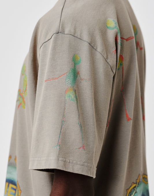 A close-up of a persons shoulder and upper arm wearing the LIVE FAST DIE YOUNG Died for It Tee in taupe, made from 100% Baumwolle, with colorful abstract skeleton graphics on the sleeve and upper chest. The face is not visible.