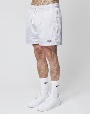 A person with tattooed legs wears LIVE FAST DIE YOUNG Basic Satin Shorts in a regular fit, white LFDT crew socks, and white Nike sneakers, standing against a plain light background.