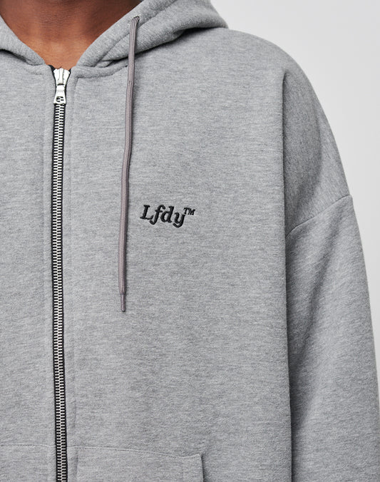 A person wears a light grey LFDY Hooded Zip hoodie, featuring a small black LFDY™ logo-stick on the left chest. Only their lower face and upper body are visible. The double-layered hood adds extra comfort.