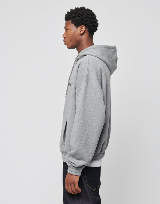 A young man stands in profile against a plain light background, wearing the LFDY Hooded Zip oversize gray hoodie with the hood down and dark jeans.