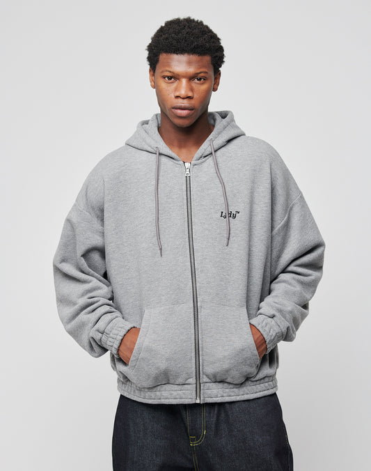 A young man with short curly hair stands against a light background, wearing the LFDY Hooded Zip gray hoodie with a doppellagige Kapuze and hands in the pockets, looking directly at the camera with a neutral expression.