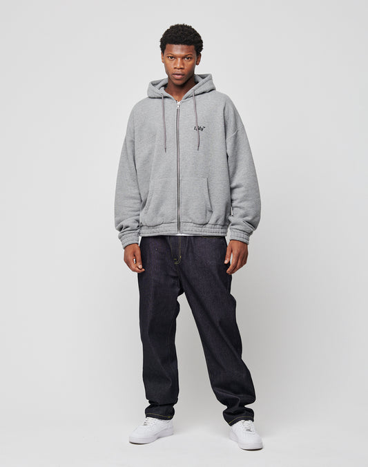 A young man stands against a plain white background, wearing an LFDY Hooded Zip in light gray with doppellagige Kapuze, paired with dark blue jeans and white sneakers. He faces the camera neutrally with his hands by his sides.
