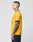 A person with short hair and visible tattoos stands in profile, wearing the LIVE FAST DIE YOUNG Survival Tee in yellow with black details and black shorts against a plain light gray background.