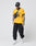 A person in the yellow LIVE FAST DIE YOUNG Survival Tee with Raglan sleeves and Relaxed Fit, black cap, crossbody bag, black pants, and white sneakers stands against a plain light background.
