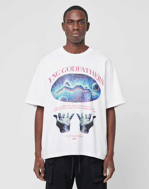 A man wears the YNG Godfathers Tee by LIVE FAST DIE YOUNG, a white oversized 100% cotton shirt with colorful abstract graphics, YNG GODFATHERS text, two hands, a cosmic scene, and a vintage effect on the front.
