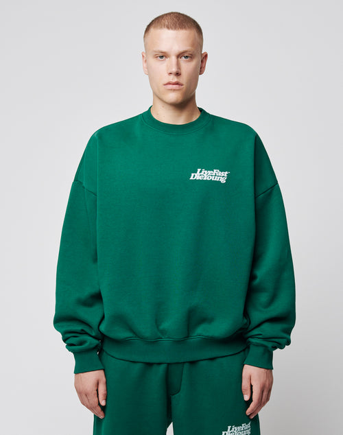 A person with short hair and a neutral expression wears the LIVE FAST DIE YOUNG Basic Chest Sweater and matching pants, featuring a subtle white chest print, against a plain light gray background.