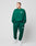 Against a plain background, a person wears an oversized green LIVE FAST DIE YOUNG Basic Chest Sweater aus Baumwolle with matching sweatpants and white sneakers. Both top and pants have small white chestprint logos on the front.