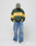 A person wears the LIVE FAST DIE YOUNG New World Sweater in green and yellow with loose ripped blue jeans, white sneakers, and a green cap, standing against a plain white background looking down with hands in the sweater pocket.