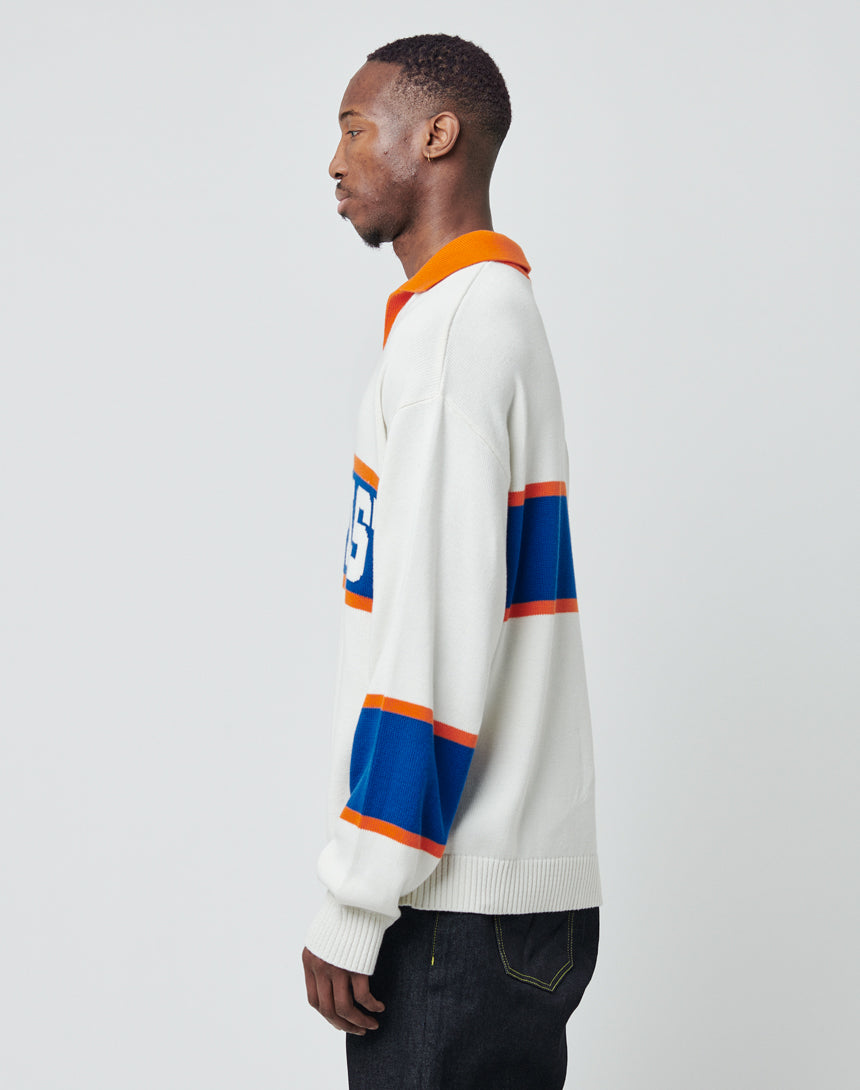A man stands in profile against a plain background wearing the LFDY Knit Polo by LIVE FAST DIE YOUNG, an oversize pullover with orange and blue stripes on the sleeve and chest, number 95, a polo collar, and dark jeans.