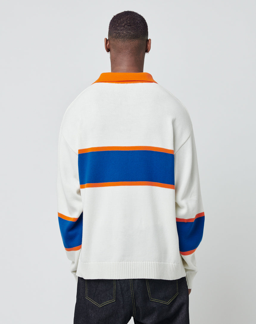 A person faces away wearing the LFDY Knit Polo by LIVE FAST DIE YOUNG, featuring blue and orange horizontal stripes with an orange polo collar. The white sweater is paired with dark jeans against a plain, light backdrop.