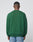 A person with short hair stands with their back to the camera, wearing a green LIVE FAST DIE YOUNG Y Knit Sweater in Oversize Fit and light blue jeans against a plain light gray background.