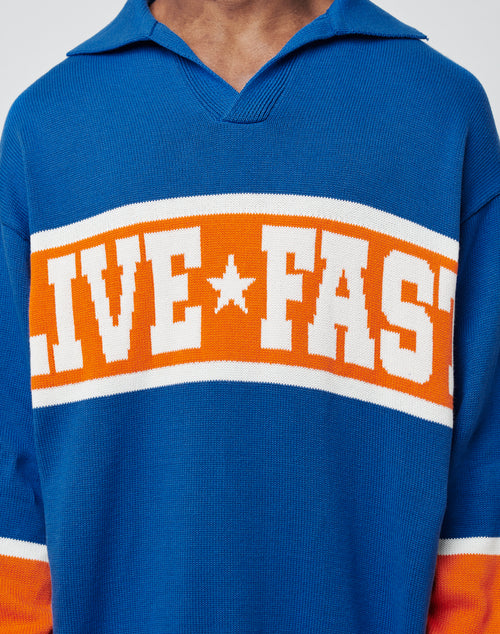 A person wears an LFDY Knit Polo by LIVE FAST DIE YOUNG in blue, with orange and white chest stripes and bold white "LIVE FAST" lettering separated by a star. The striking knit design stands out, with the face partially out of frame.