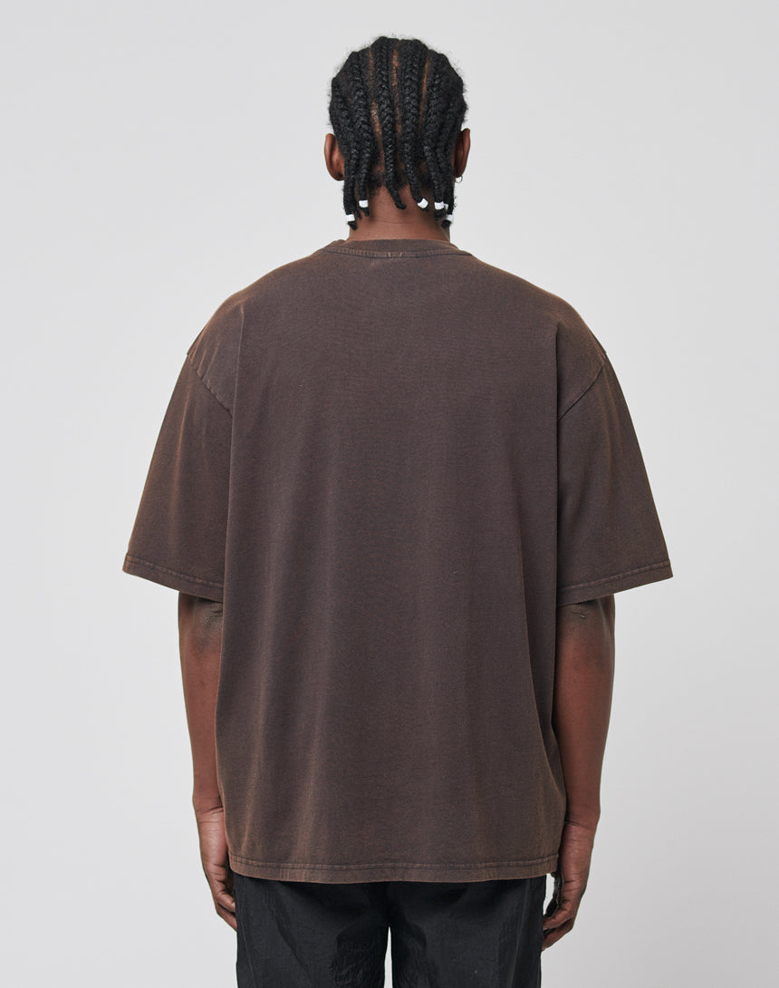 A person with braided hair faces away from the camera, wearing black pants and an Eagle Tee by LIVE FAST DIE YOUNG against a plain light gray background.