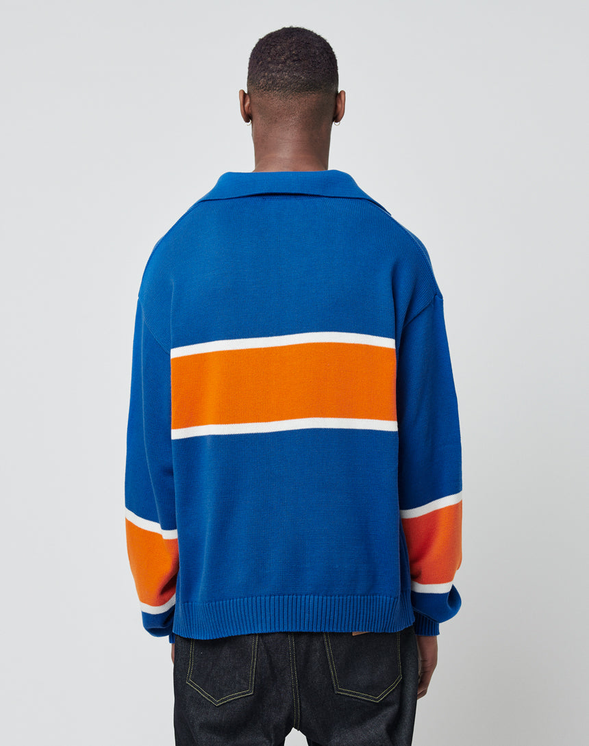 A person faces away, wearing the LIVE FAST DIE YOUNG LFDY Knit Polo featuring a bold orange and white horizontal stripe across the back and sleeves. The background is plain and light-colored.