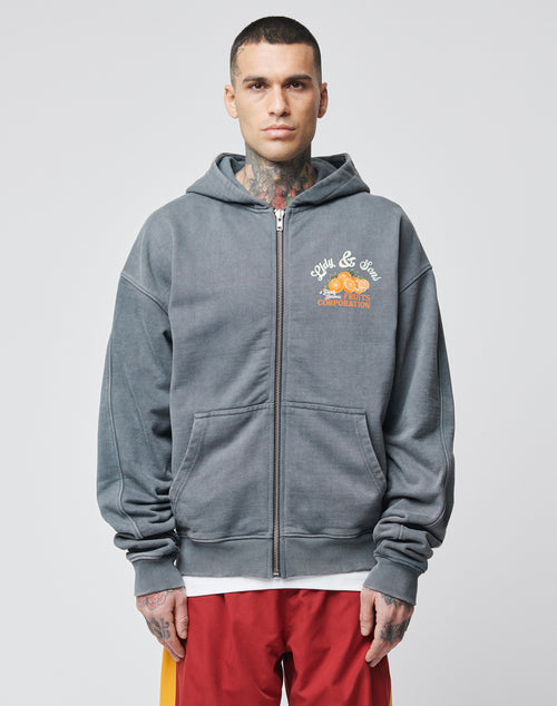 A man with short hair and tattoos wears the LIVE FAST DIE YOUNG Lfdy & Sons Hooded Zip in gray over a white shirt, paired with red shorts with yellow stripes, standing against a plain light background.